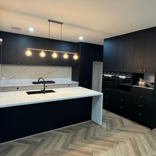 Renovated kitchen with matte black cabinetry, a stone waterfall island and pendant lighting